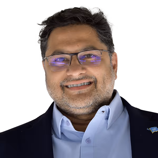 Smiling man with glasses and a beard wearing a light blue shirt and dark blazer with a pin.