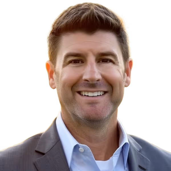 Smiling man with short brown hair wearing a gray blazer and blue shirt against white background.
