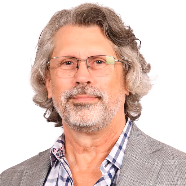 Man with medium-length gray hair, beard, glasses, checkered shirt, and gray plaid blazer.