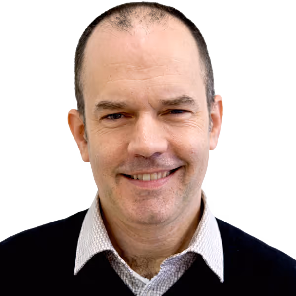 Smiling middle-aged man with short dark hair wearing a collared shirt and black sweater.