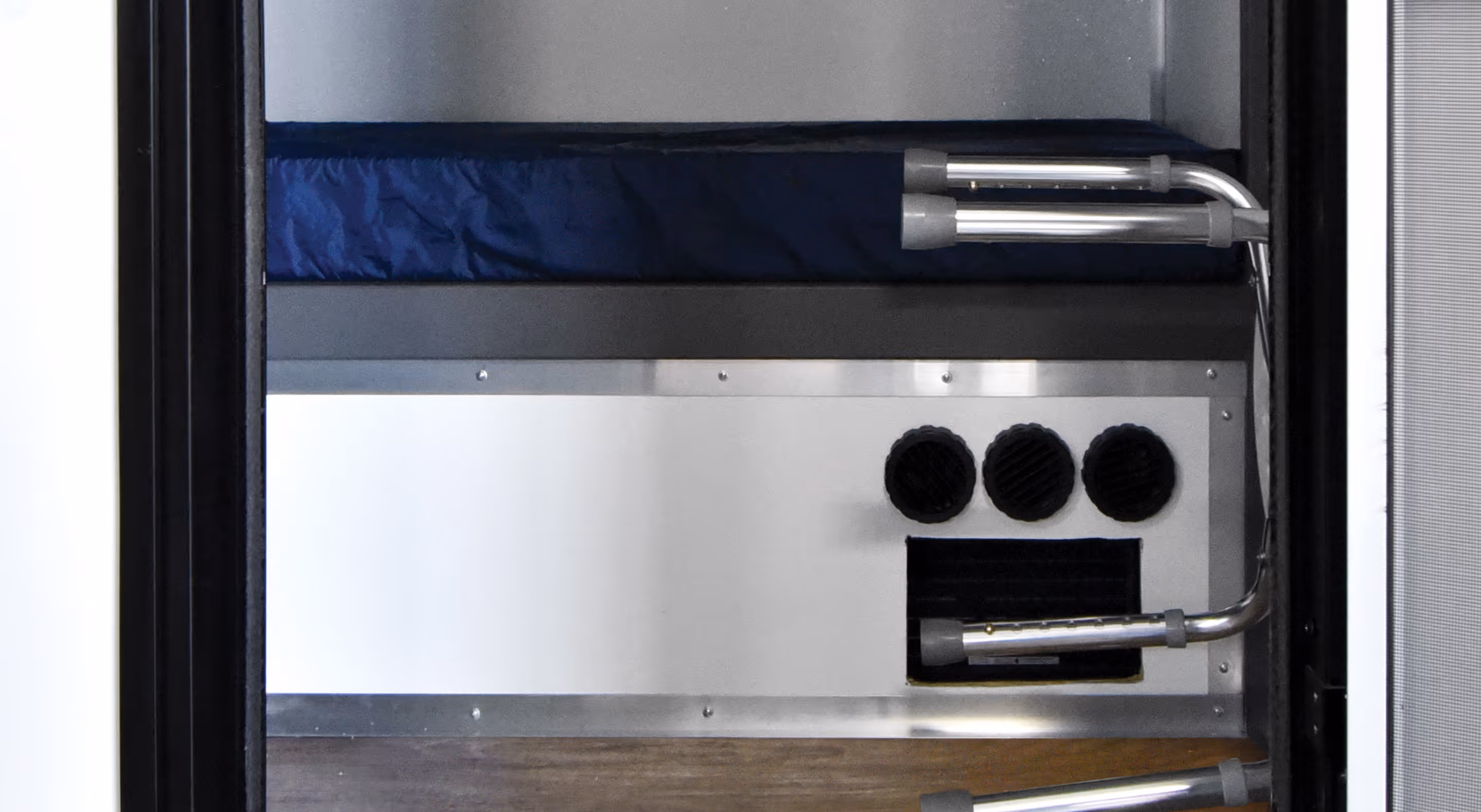 Interior of a privacy bunk with a dark blue mattress and ventilation ducts on the wall.