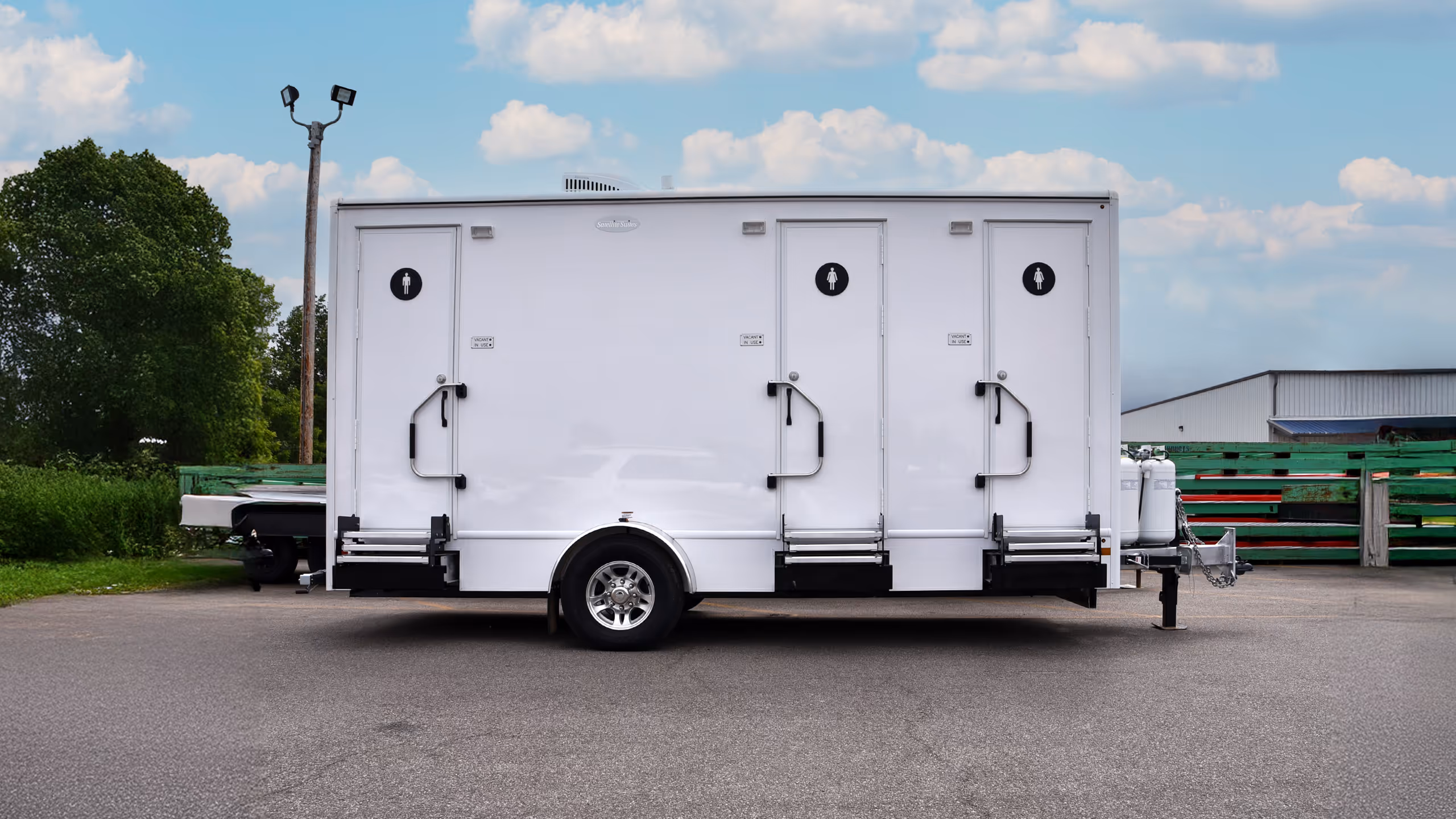 A white, double restroom trailer with three stalls parked on a paved area.