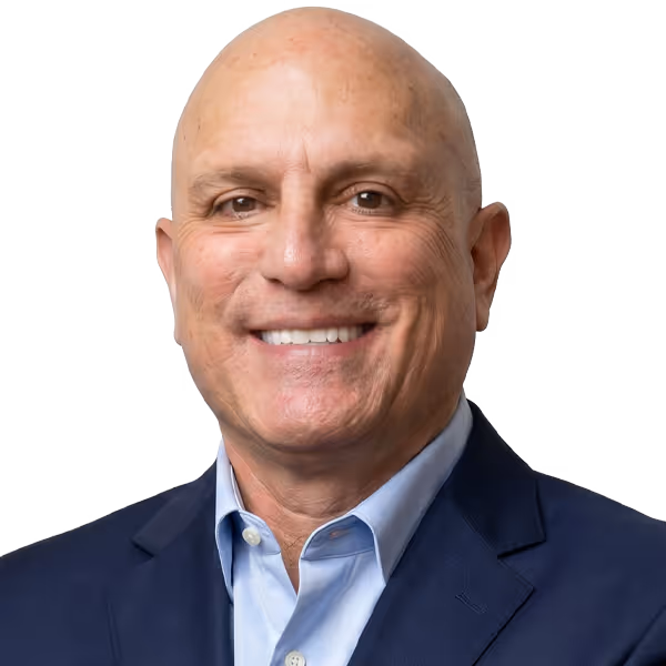 Smiling bald man wearing a dark blazer and light blue dress shirt against a white background.