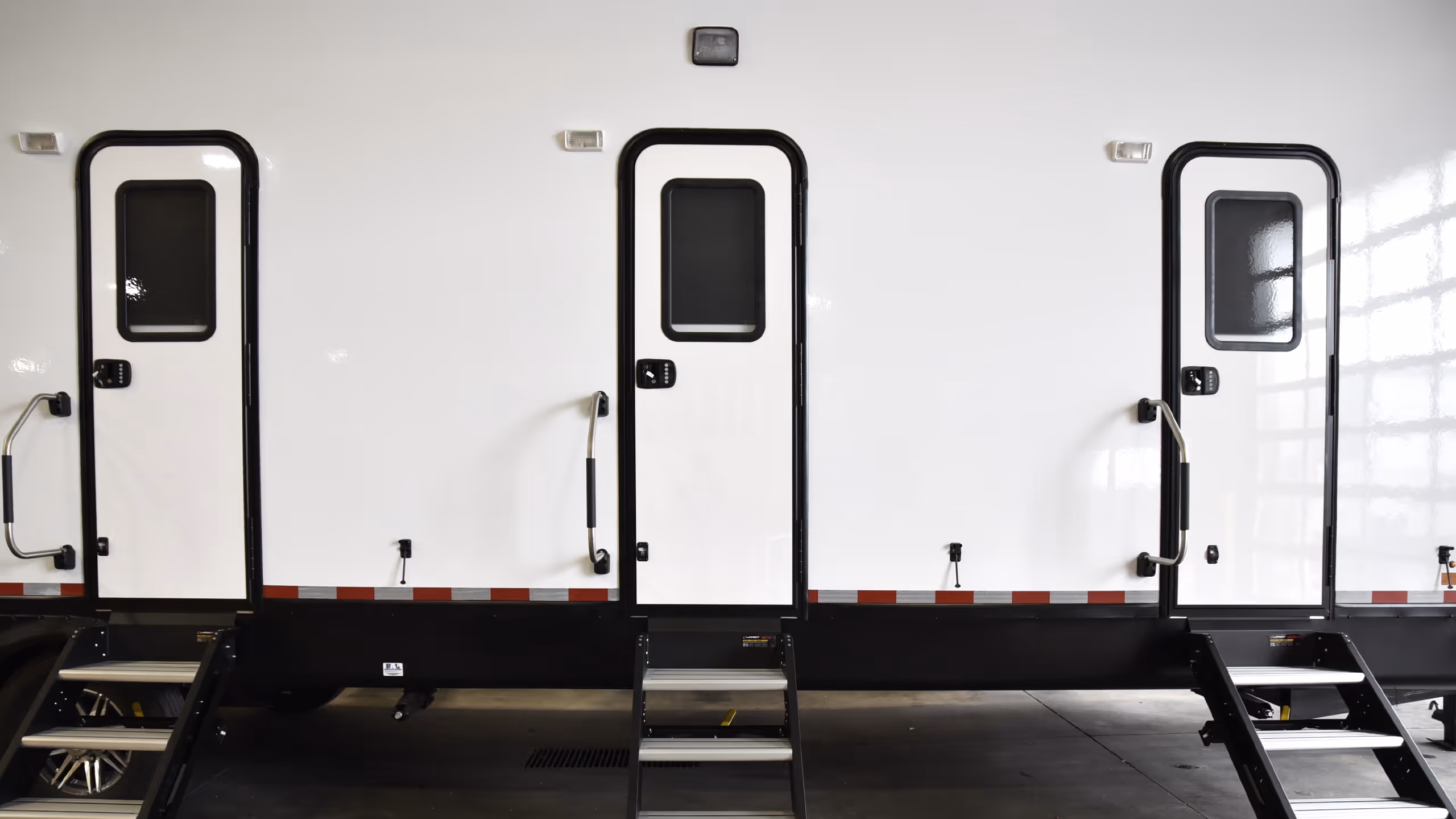 Three entrance doors on a white trailer, with steps leading up to each door.