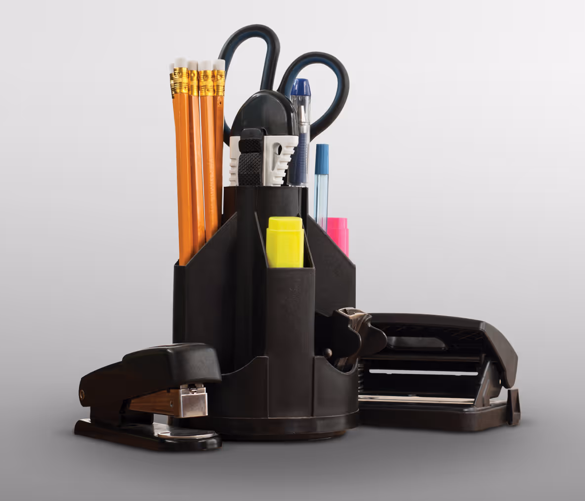 A black desktop organizer holding pencils, pens, scissors, and a stapler.