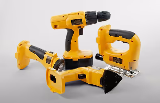 Three yellow power tools: a cordless drill, a jigsaw, and a circular saw, arranged on a gray