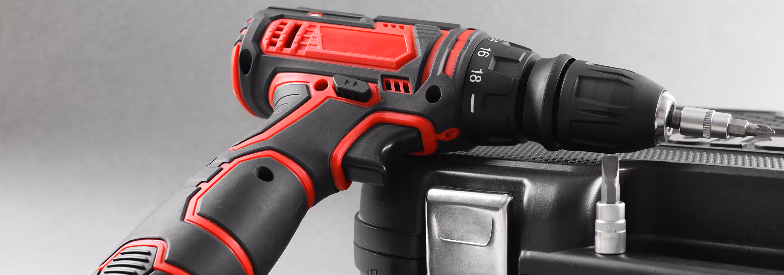 Red and black cordless power drill resting on a black tool case with a drill bit attached.