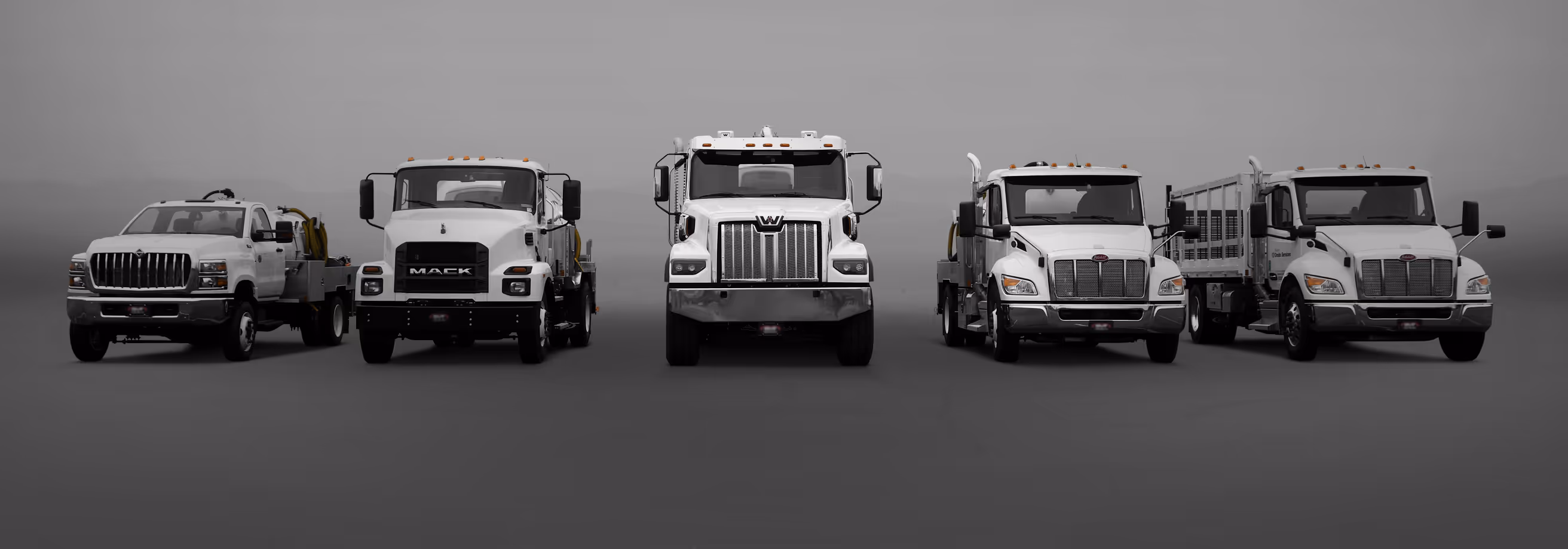 Five white heavy-duty trucks lined up side by side facing forward on a gray background.