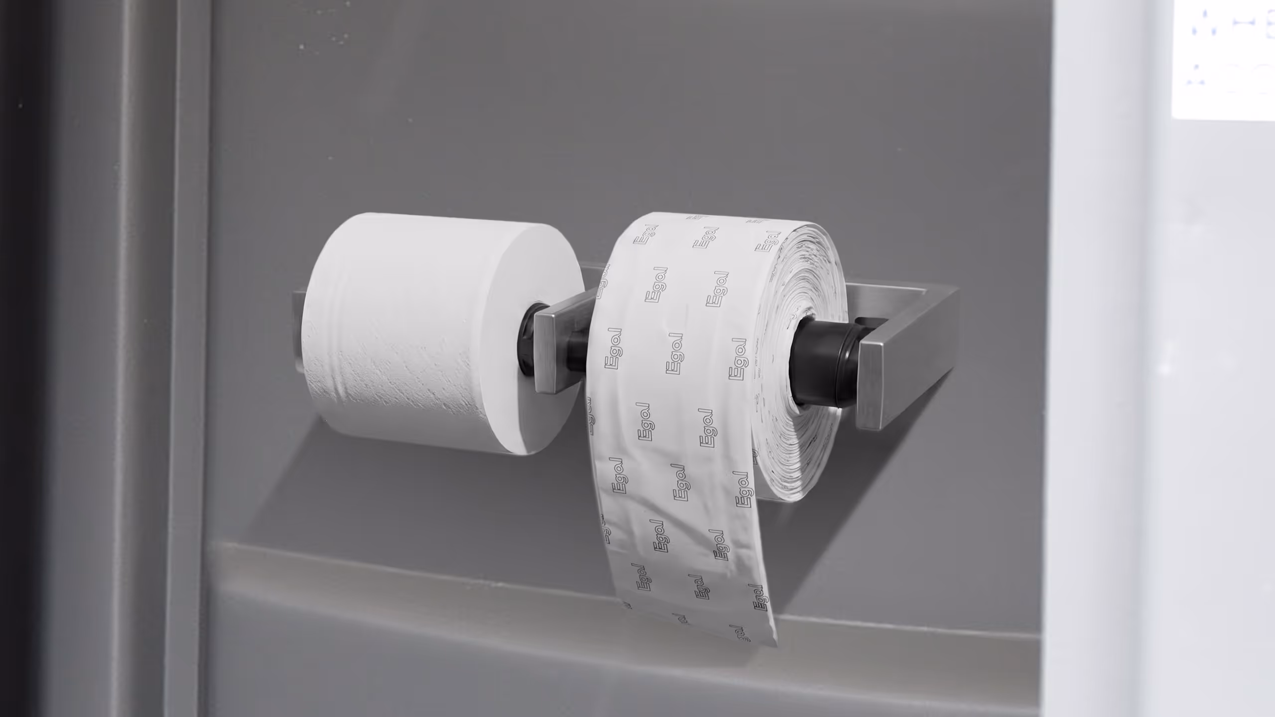 Two rolls of paper, one white toilet paper and one patterned paper, on a wall-mounted holder.