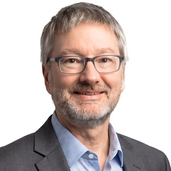 Middle-aged man with gray hair, beard, glasses, wearing a gray suit and blue striped shirt.