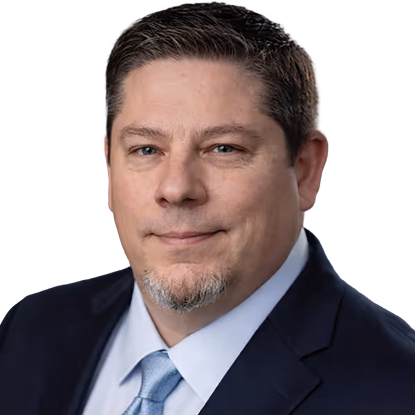 Middle-aged man with short brown hair and goatee wearing a dark suit, light blue shirt, and tie.