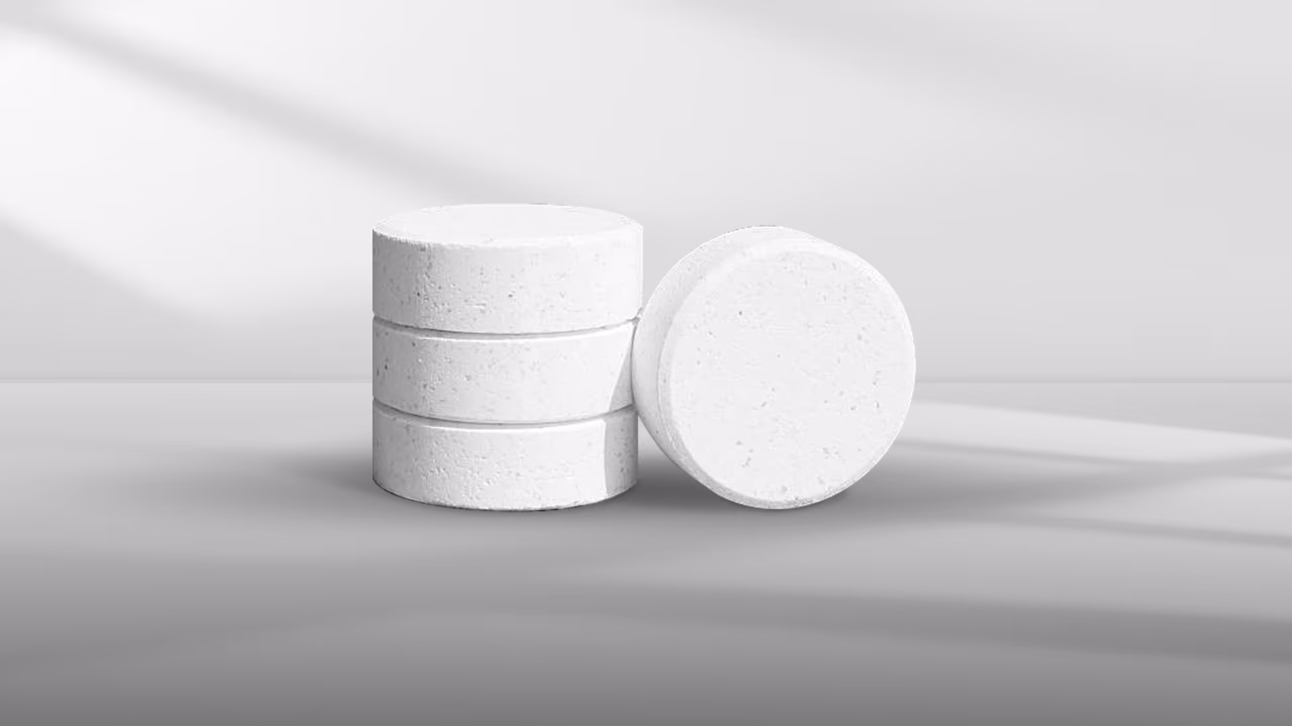 Three circular white tablets stacked with one slightly leaning on its side against a light
