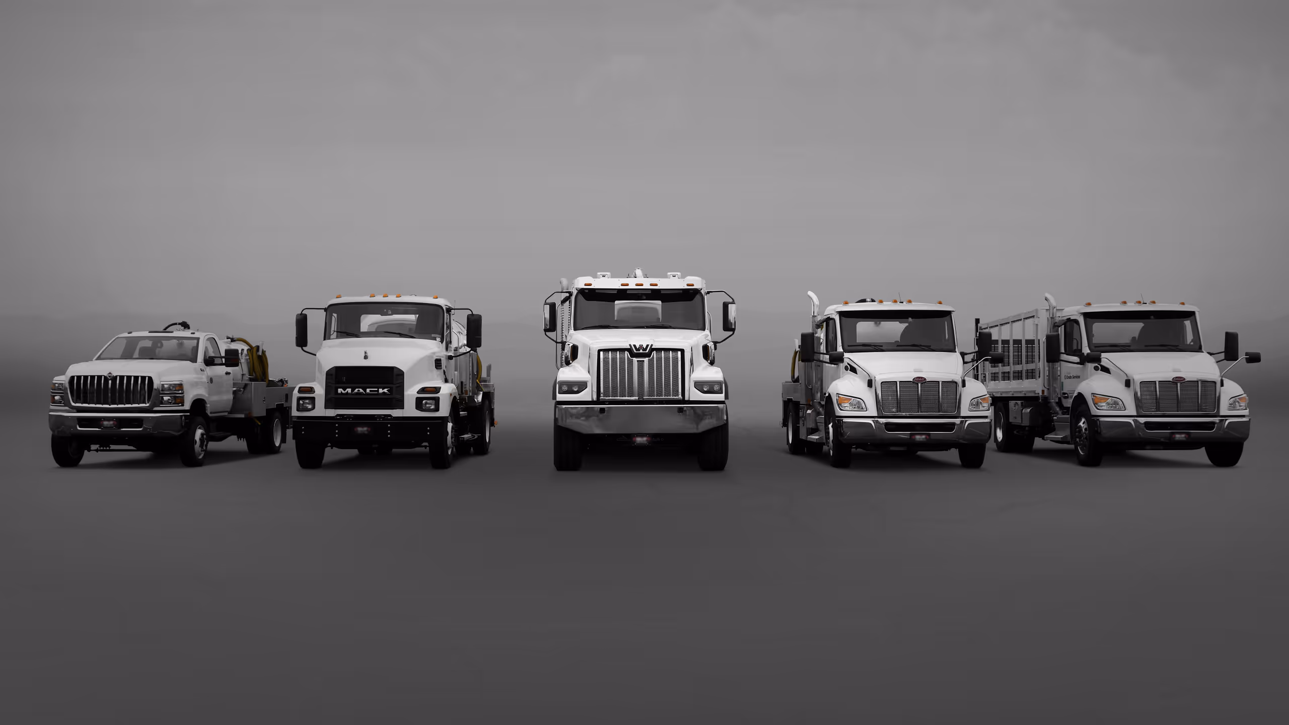 Five trucks lined up, varying in size and design, against a gray background.