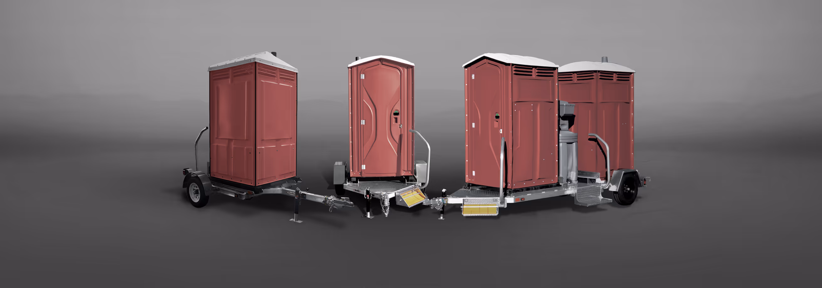 Four red portable toilets mounted on two trailers with gray floors and metal railings.