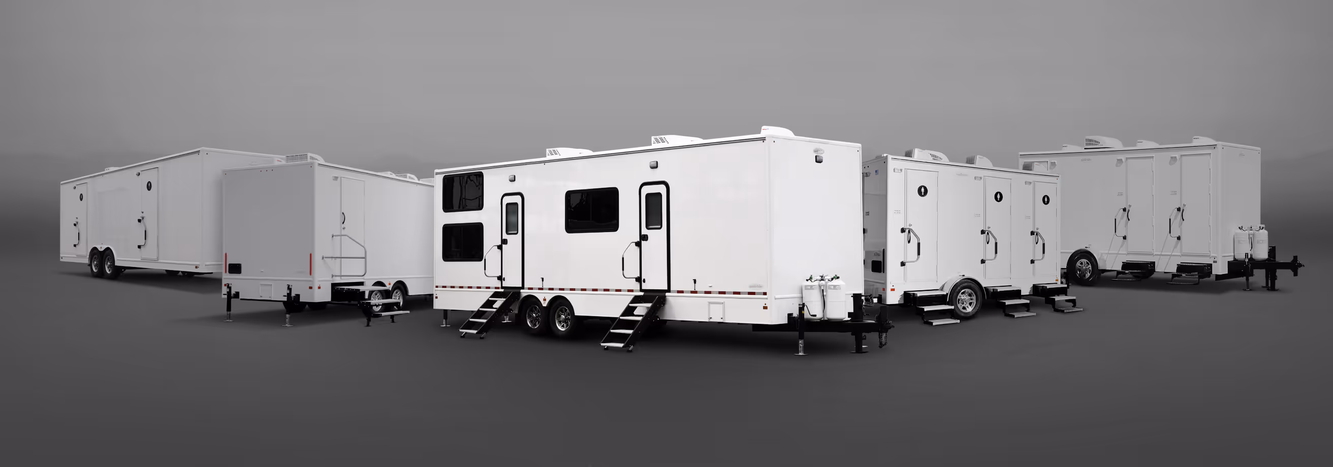 Row of large white trailers with doors, stairs, and windows on a gray background.