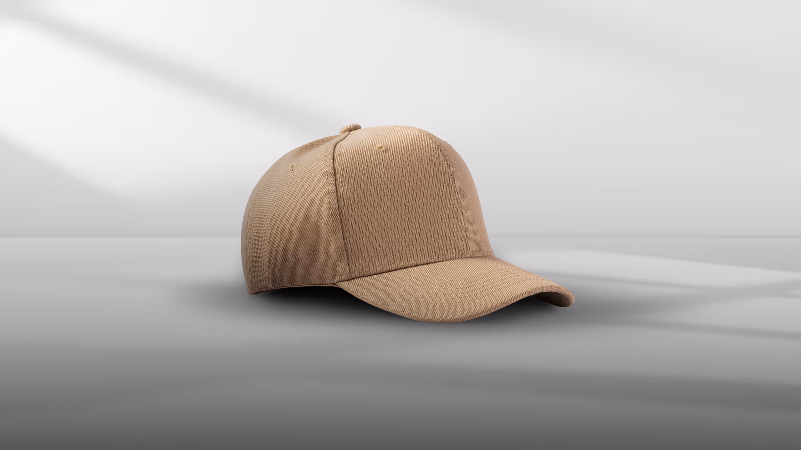 A beige baseball cap with a curved brim is positioned on a flat surface, casting a shadow.