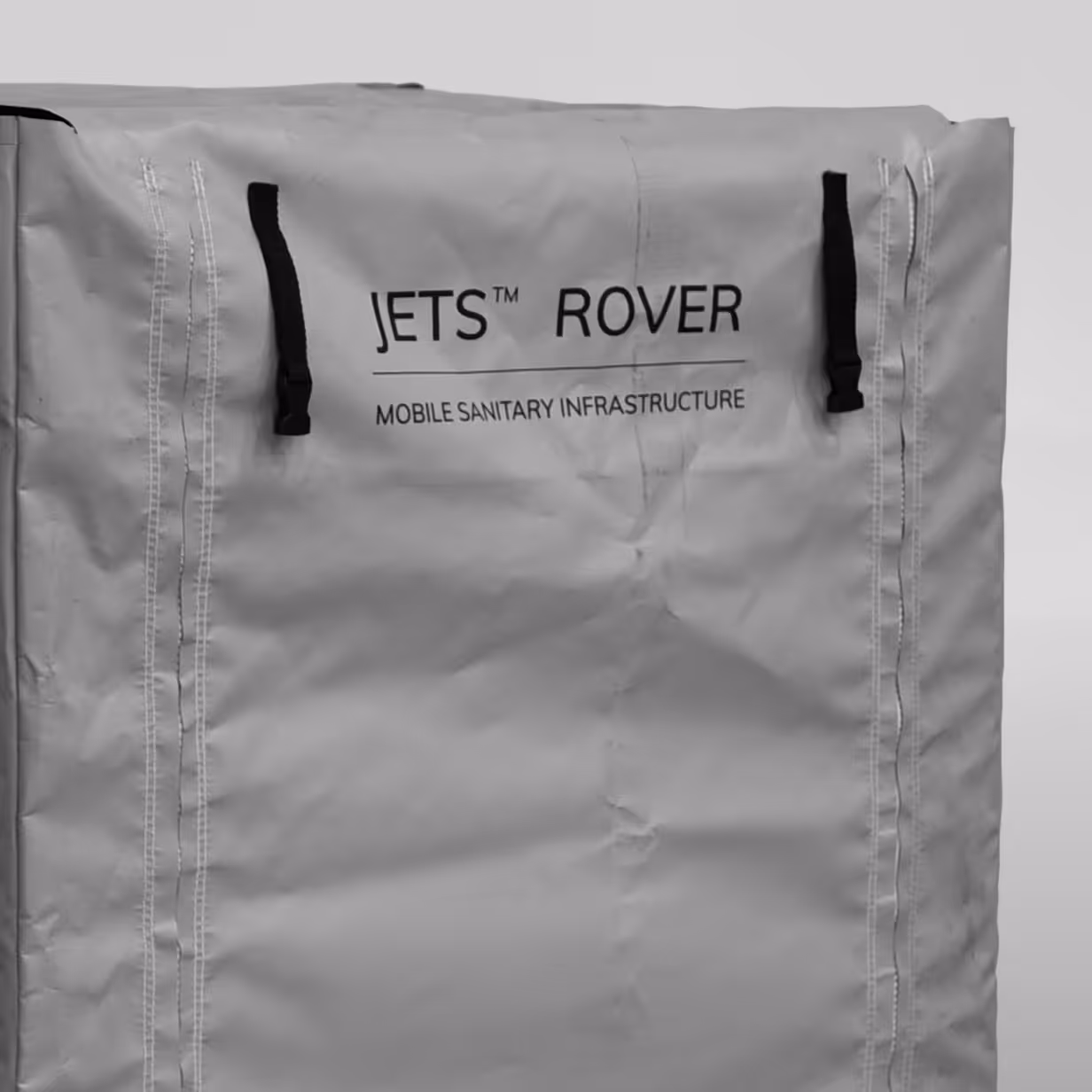 Close-up of grey tarp with black straps and text reading JETS ROVER Mobile Sanitary Infrastructure.