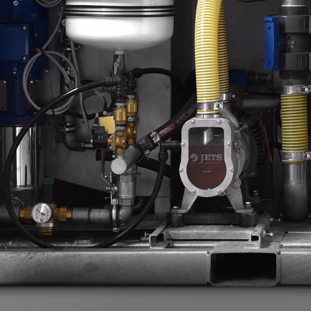 Industrial pump with yellow hoses, metal pipes, valves, and pressure gauge on a metal base.