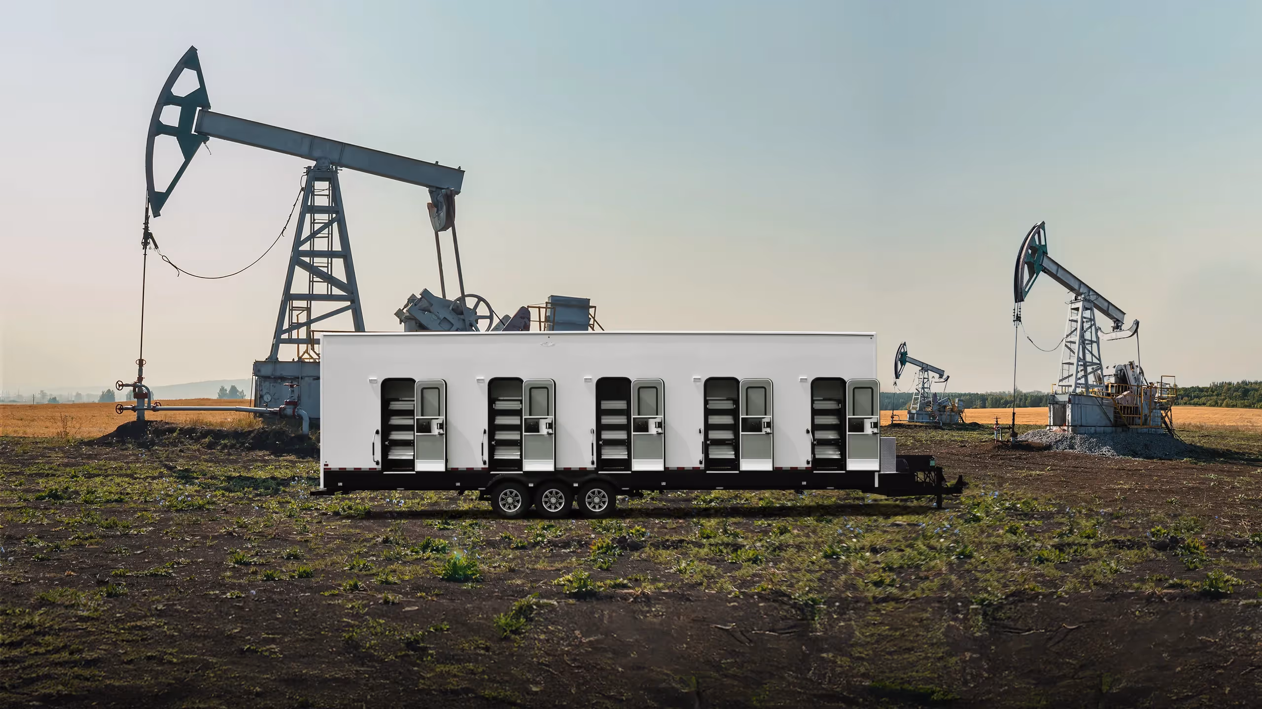 White mobile trailer with multiple open doors in a field with oil pumpjacks in the background.