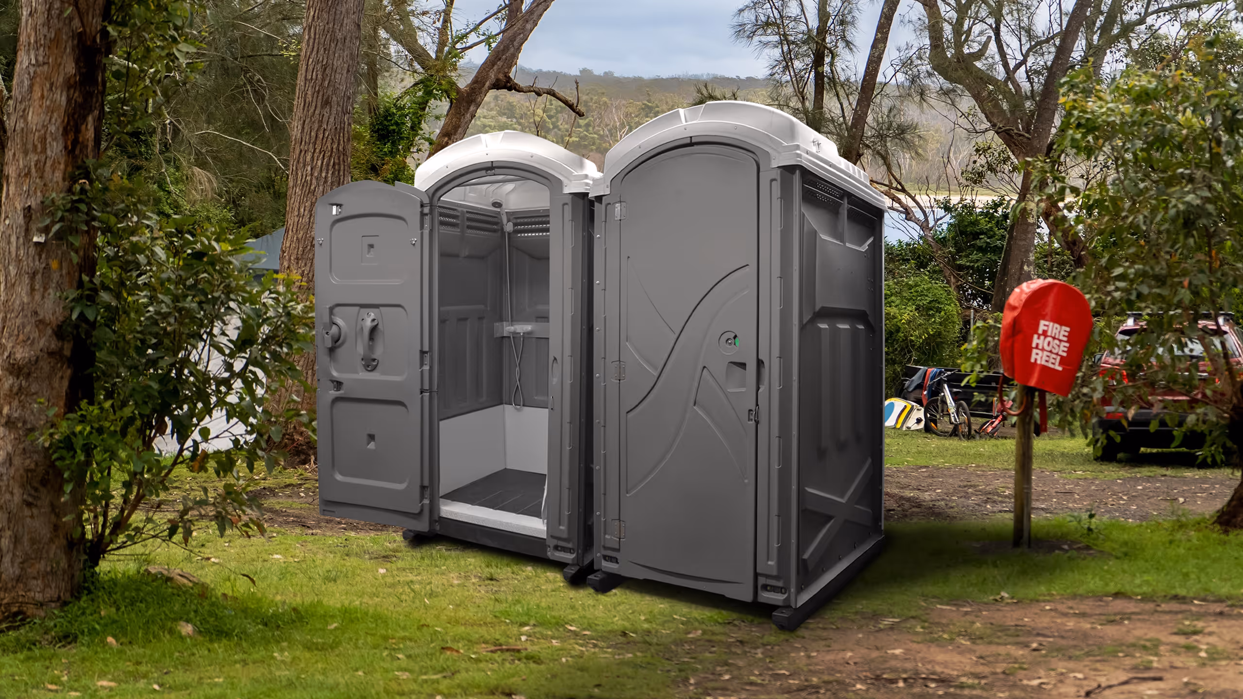 Two gray portable shower units on grass with one door open showing interior shower head.