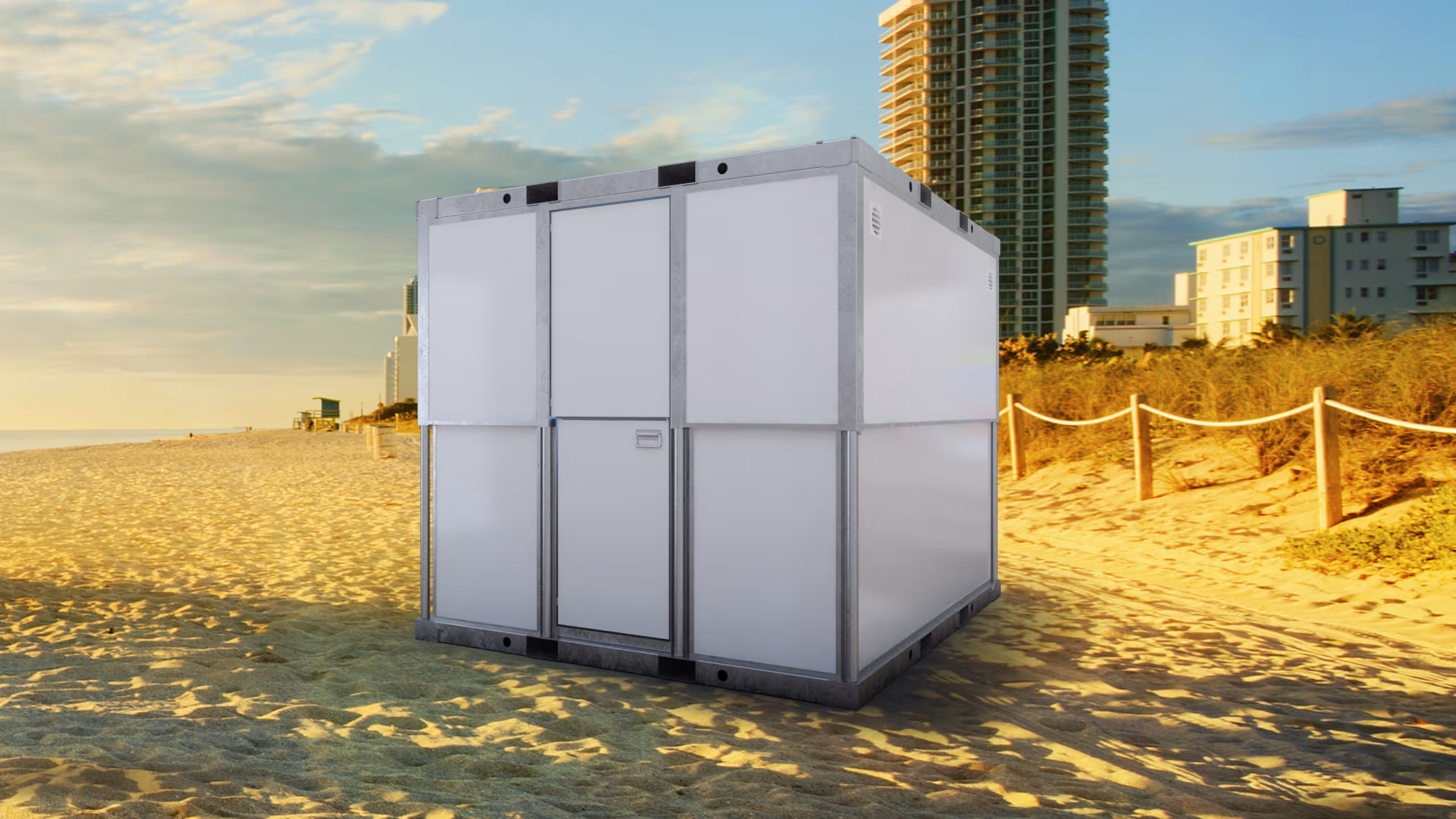 White modular container unit on a sandy beach with buildings and dunes in the background.