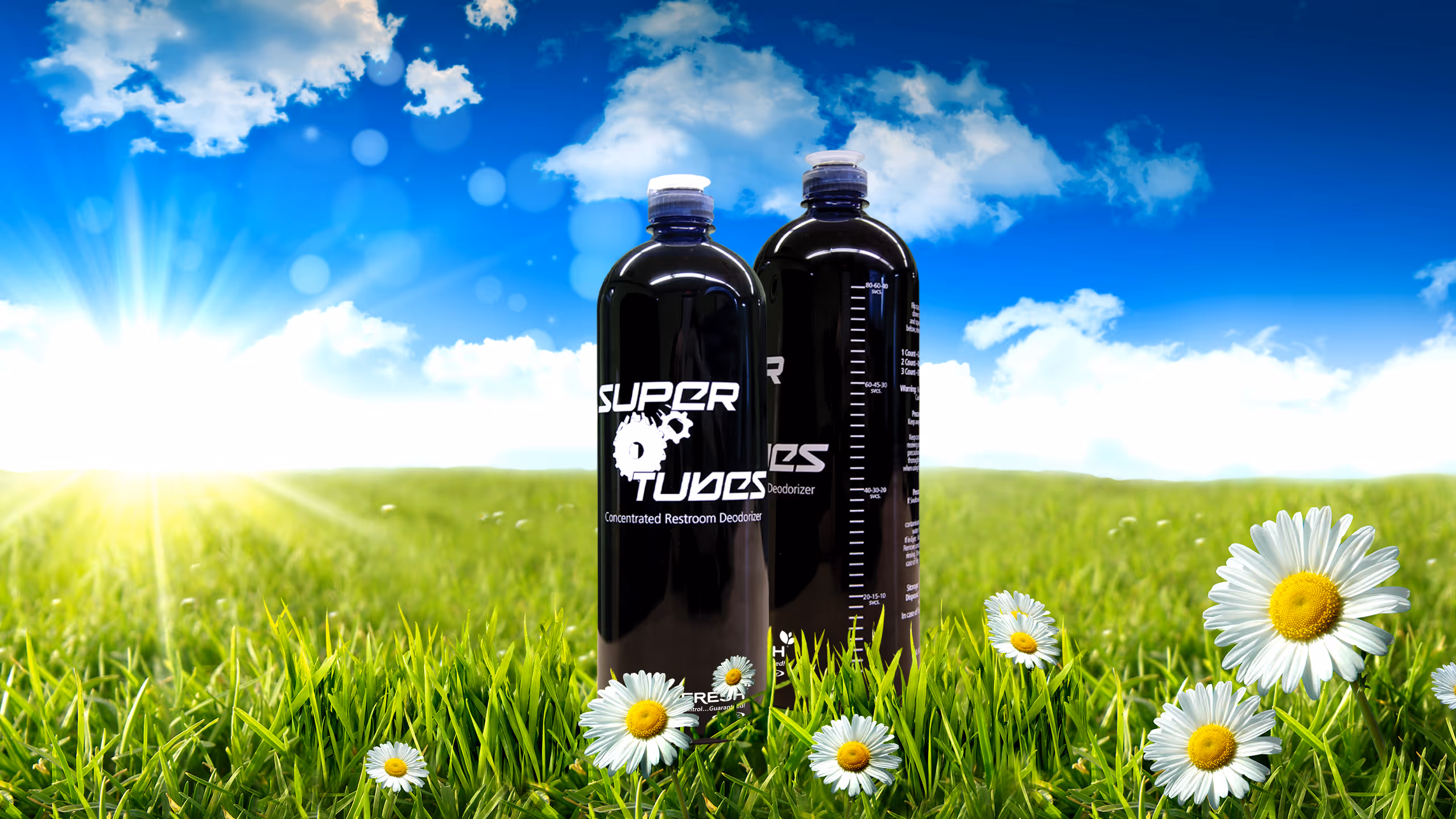 Two black bottles of Super Tubes concentrated restroom deodorizer in green grass with daisies and blue sky.