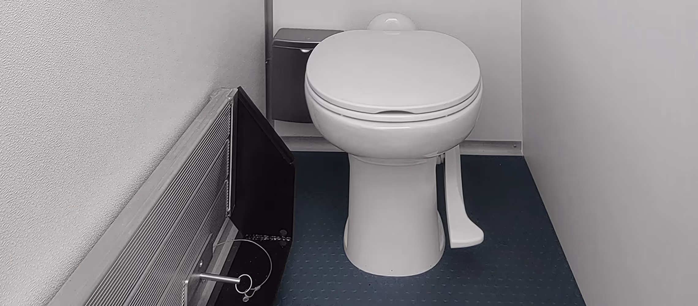 A clean white toilet in a small bathroom with gray walls and a black heater.