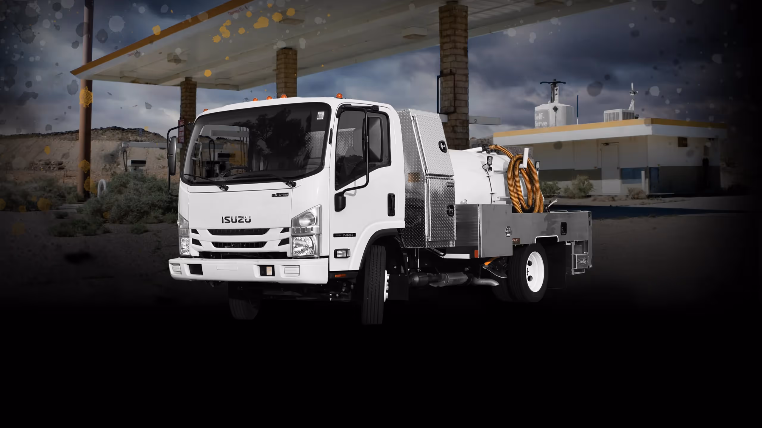 White Isuzu utility truck equipped with industrial hoses parked at a gas station.