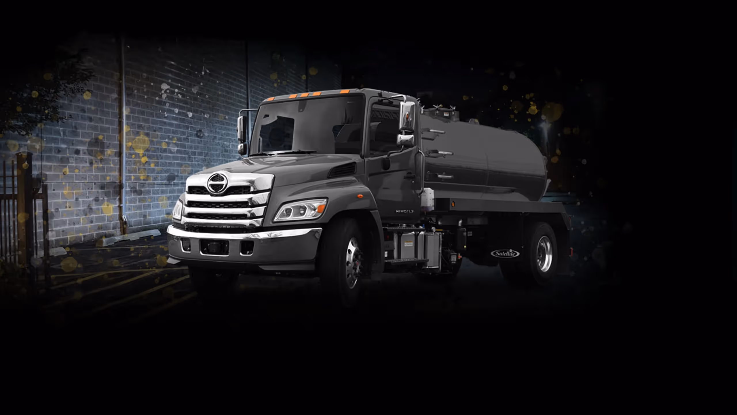Gray industrial septic service truck with large tank parked against a brick building at night.