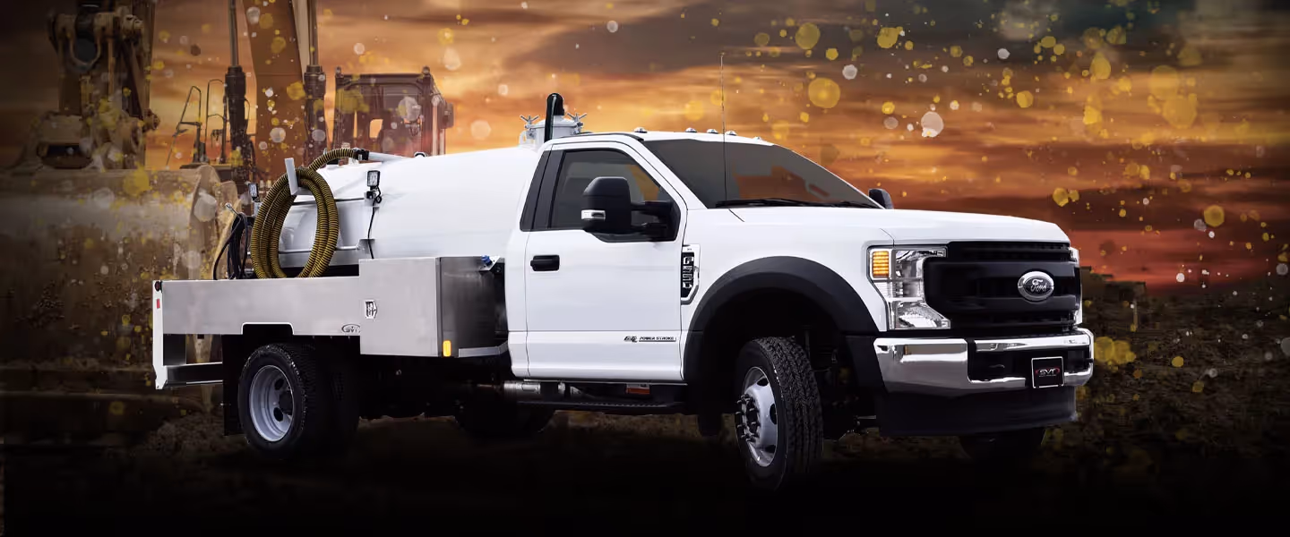 White Ford utility truck with tank and hose on the back against a sunset construction site background.