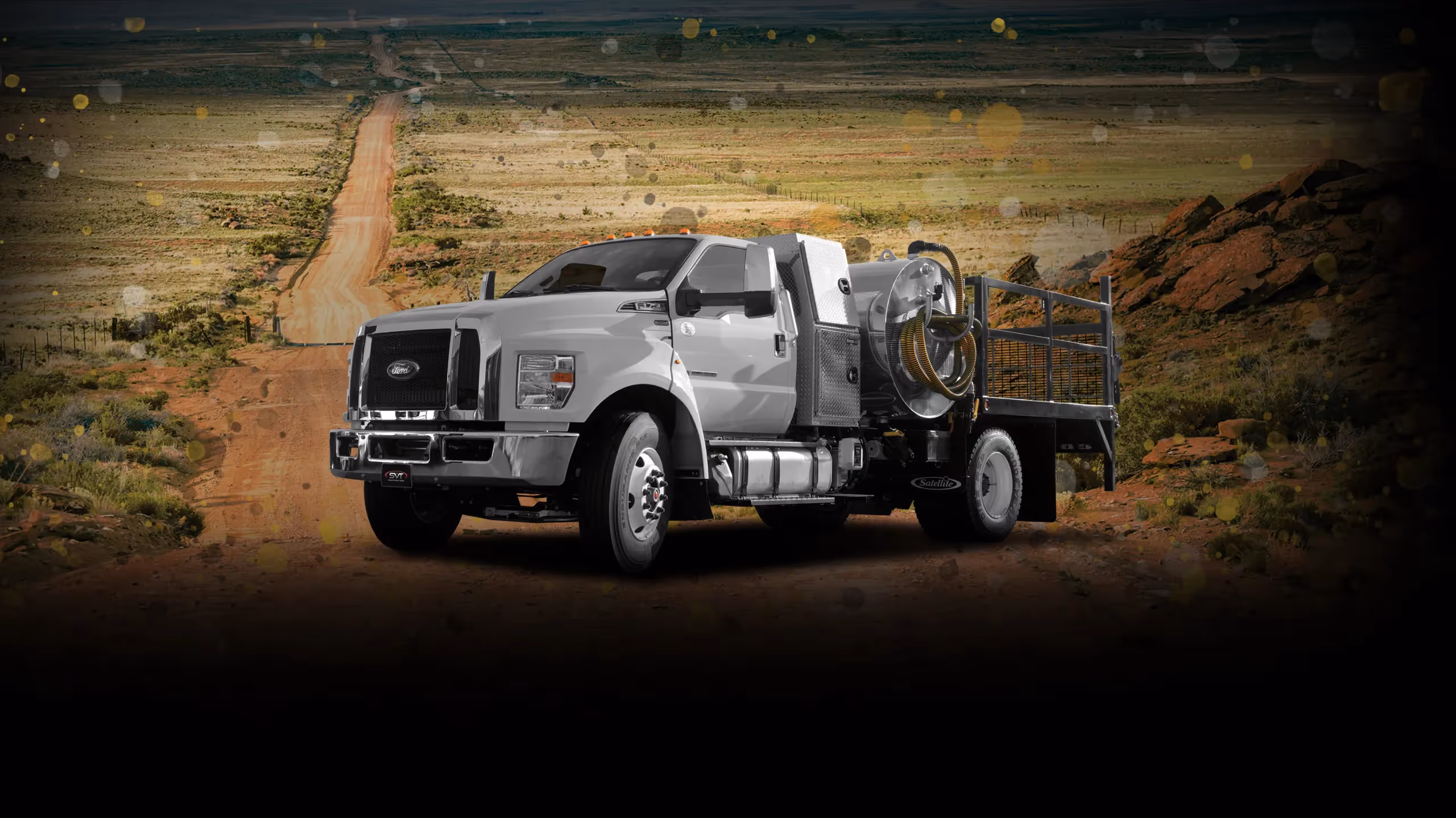 White Ford industrial truck with equipment on back parked on dirt road in rural rocky landscape.