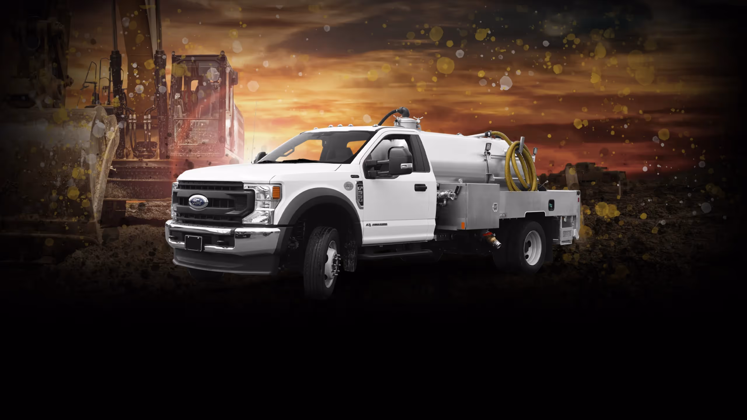 White industrial vacuum truck with large hose on the flatbed against a sunset and earthmoving equipment background.