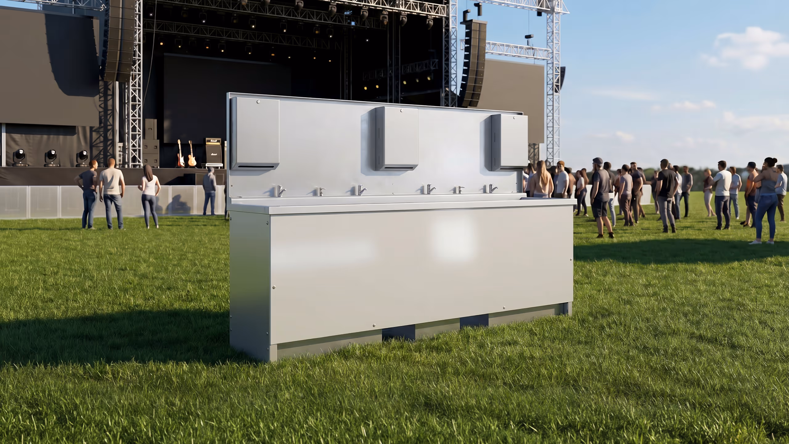 Metal hand wash station with faucets on grass field near crowd and stage at outdoor event.