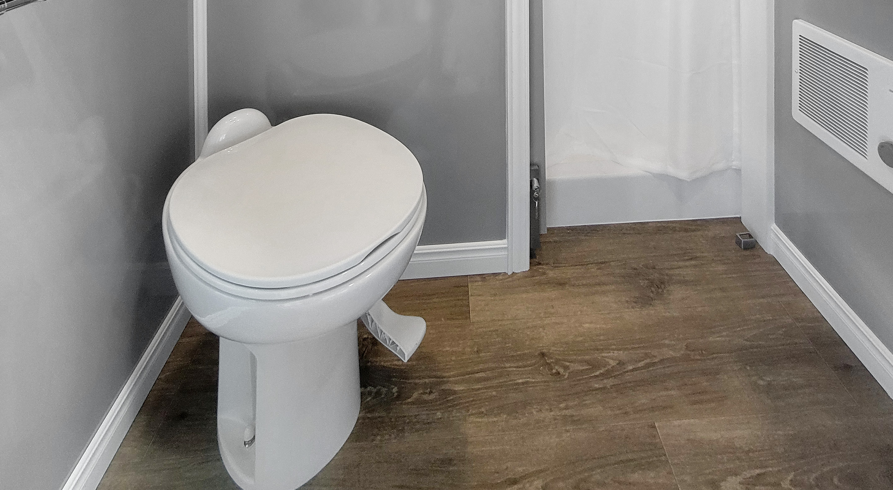 White toilet with closed lid on wood-look flooring against gray walls in a bathroom.