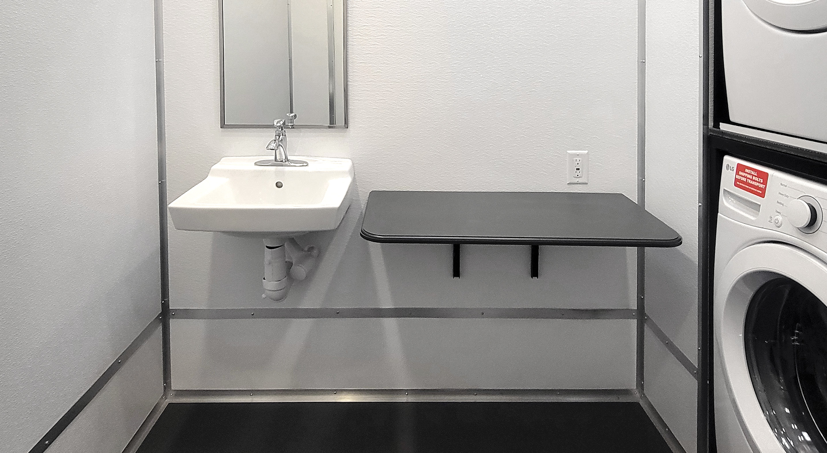 Laundry room with stacked washer and dryer, wall-mounted sink, mirror, and fold-down table.