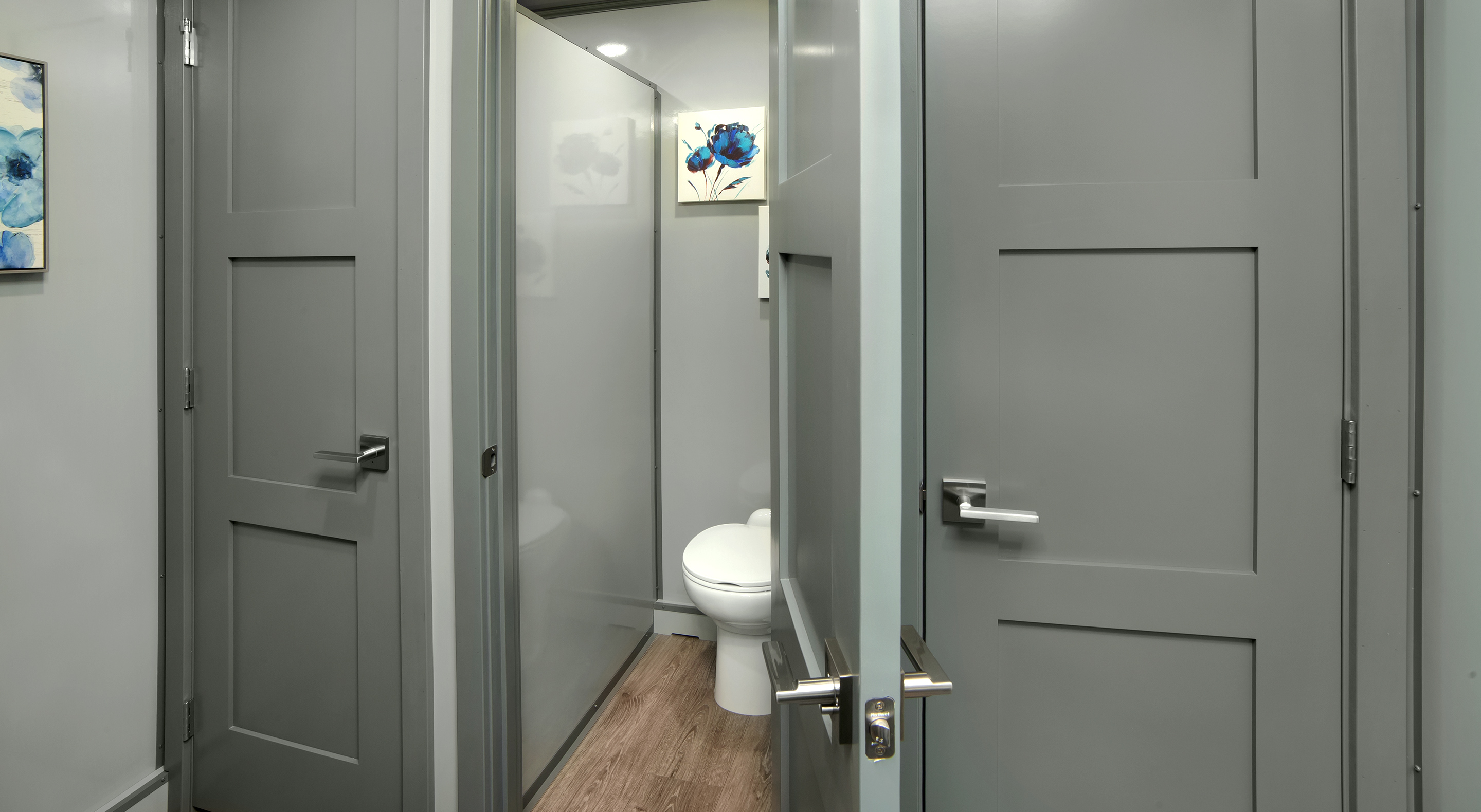 Interior view of a bathroom with gray paneled doors and a white toilet on wooden floor.