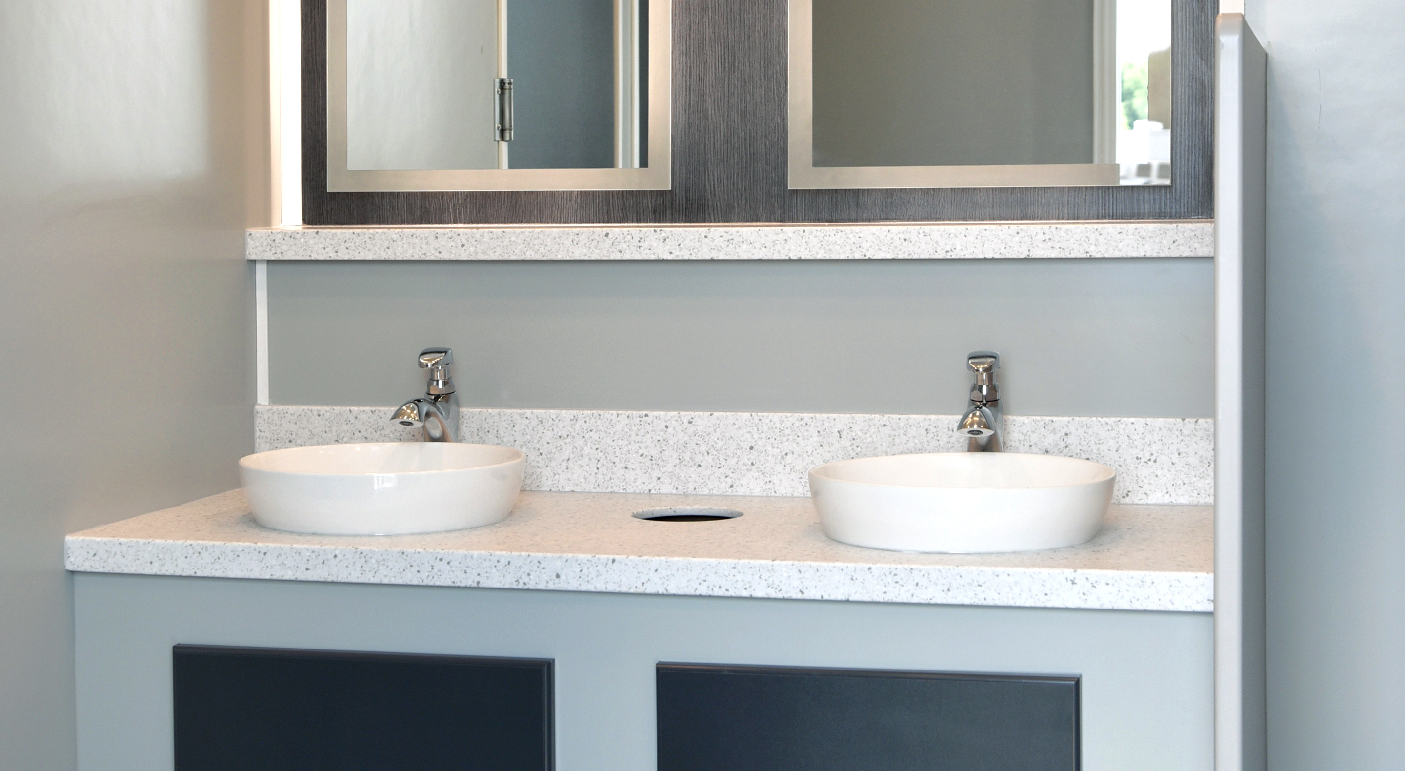Modern bathroom vanity with two white vessel sinks, gray cabinetry, and mirrored cabinets above.