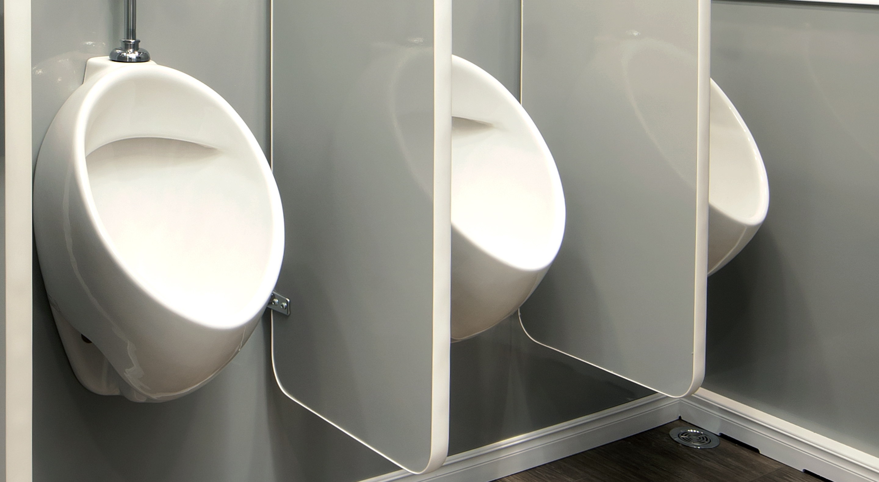 Three white urinals separated by gray privacy dividers in a public restroom.