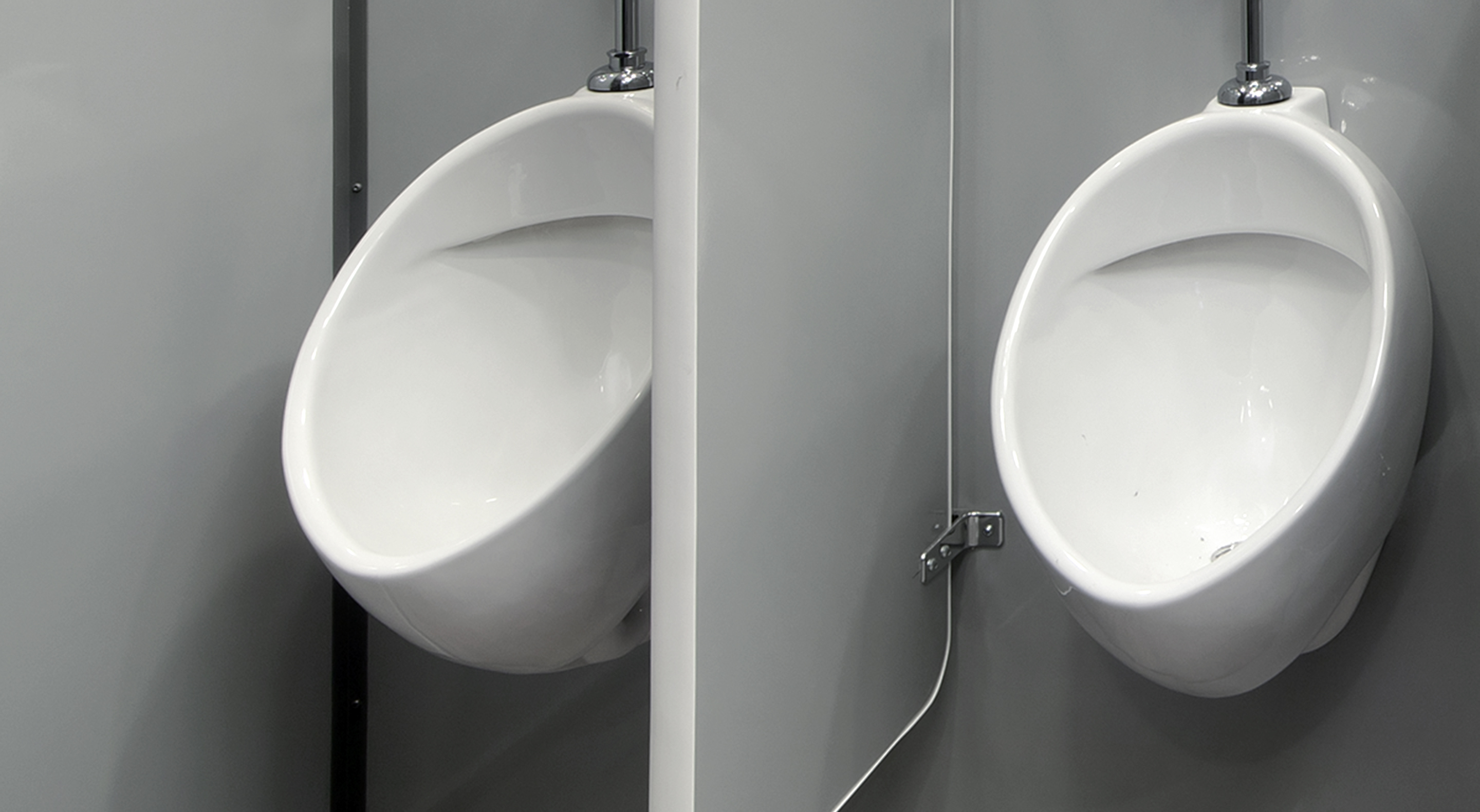 Two white ceramic urinals mounted on a gray wall with a privacy divider between them.
