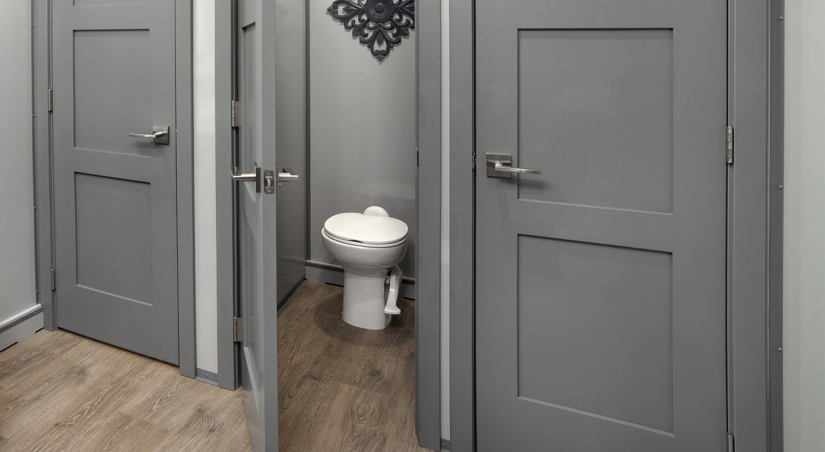 Three gray doors in a hallway, with one showing a toilet in a small bathroom visible beyond.