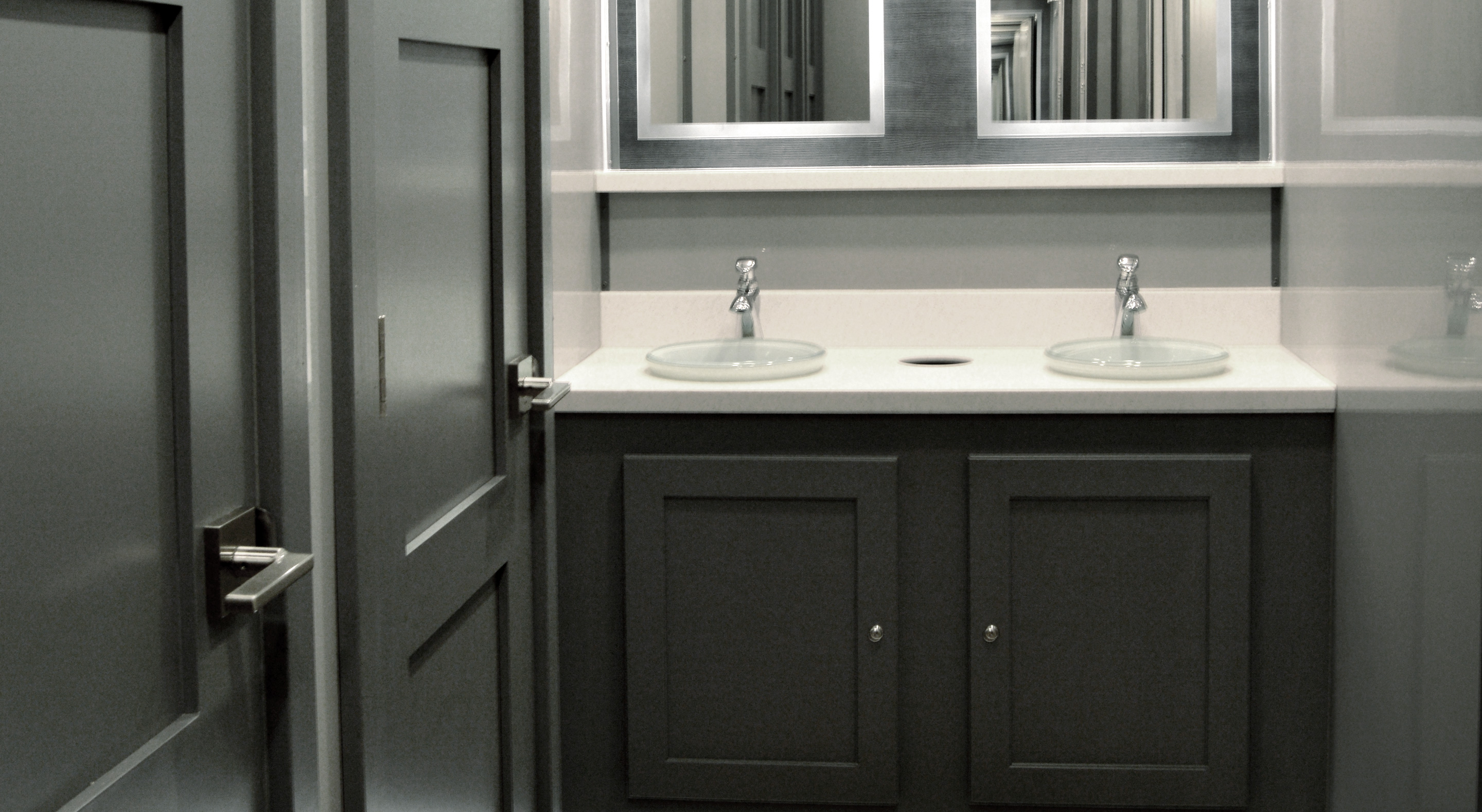 Modern bathroom vanity with two glass sinks, silver faucets, and dark cabinetry under a large mirror.