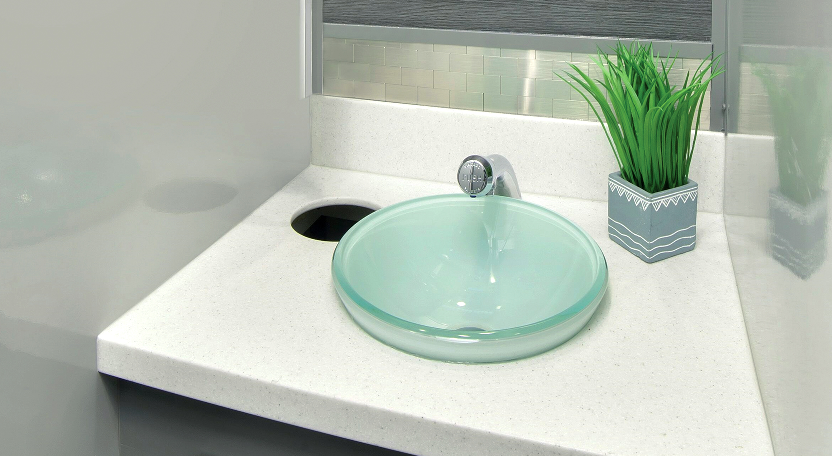 Modern bathroom sink with clear glass bowl, chrome faucet, and a small decorative potted plant.