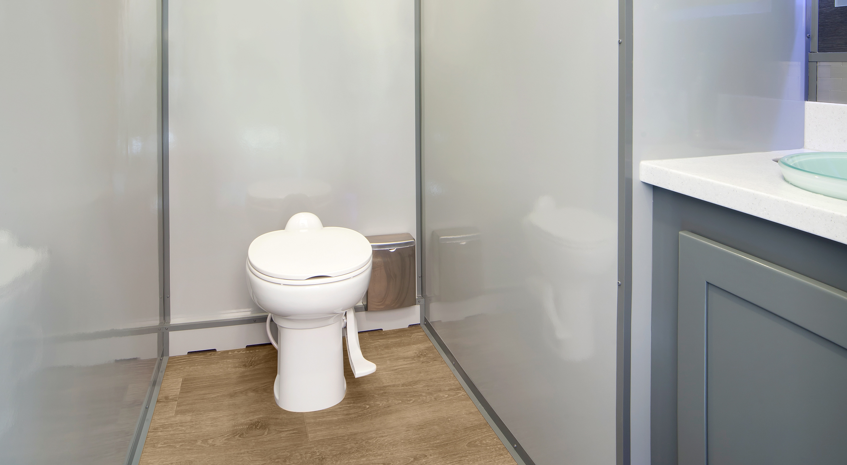 Accessible toilet with hand-operated flush pedal on wood-look floor inside a gray-walled restroom.
