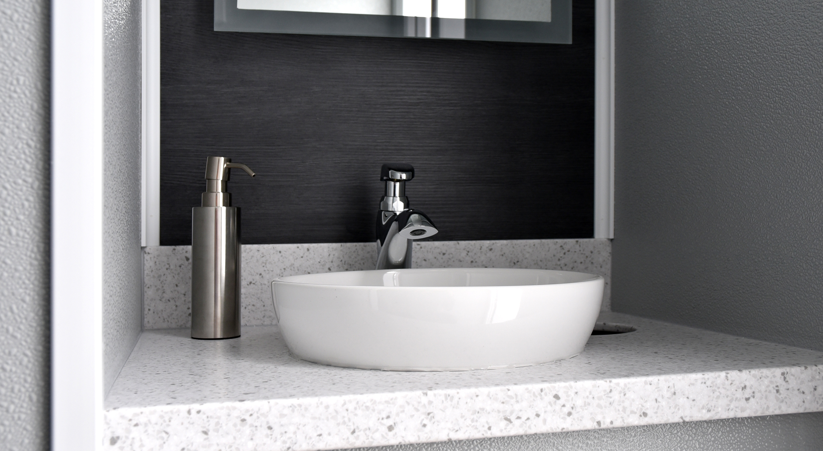 Modern bathroom sink with a sleek white bowl, silver faucet, and metal soap dispenser on a