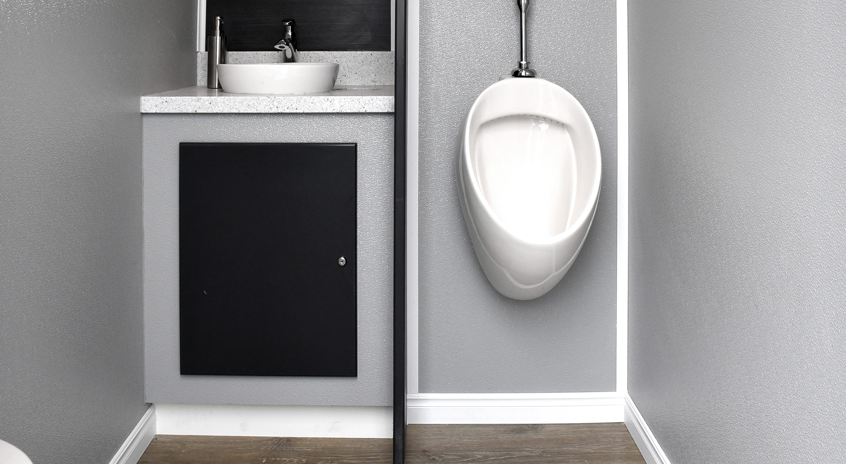 Restroom featuring a wall-mounted urinal and a sink with a countertop in a gray environment.