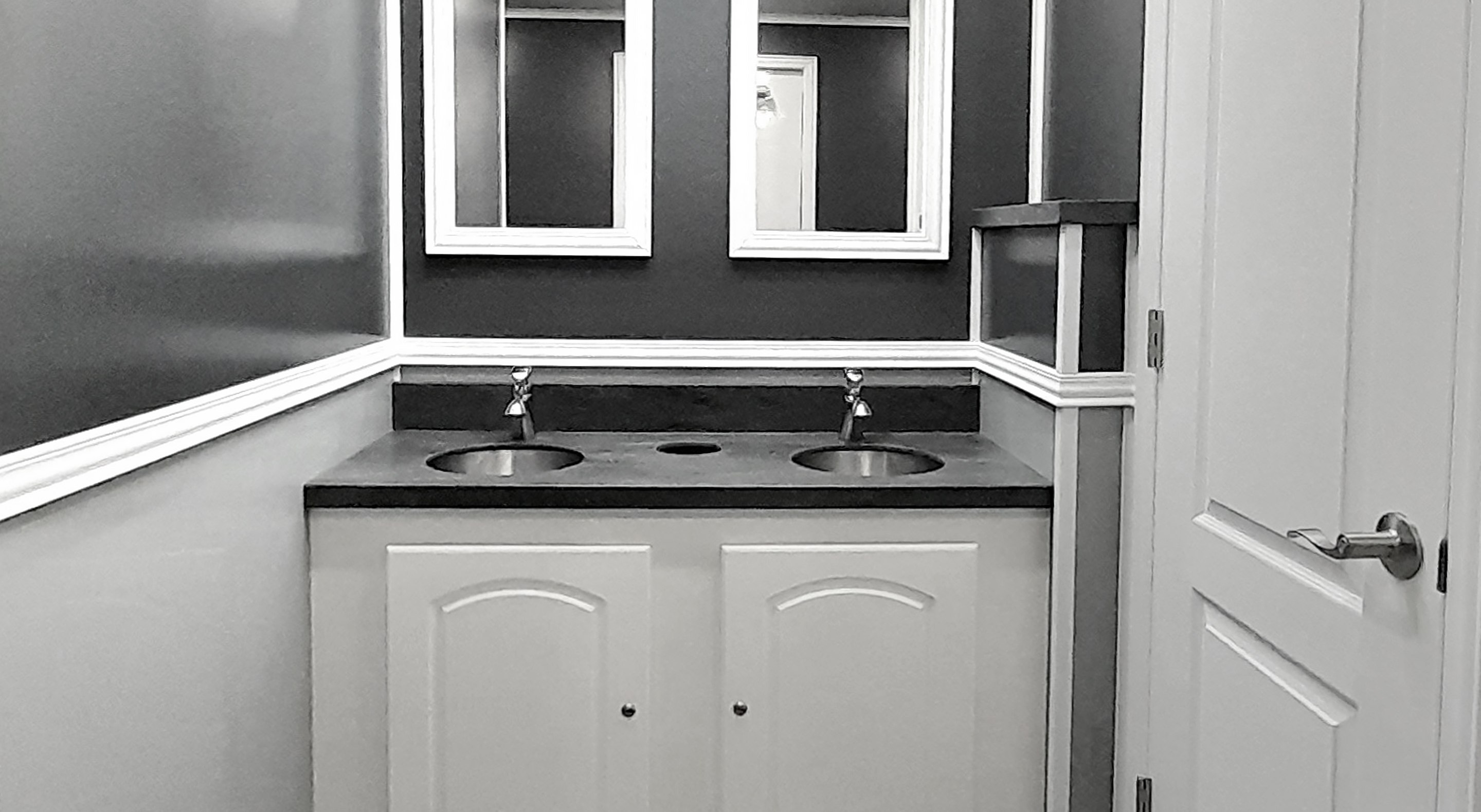 Bathroom vanity with double sinks, two mirrors above, and a partially open door on the right.