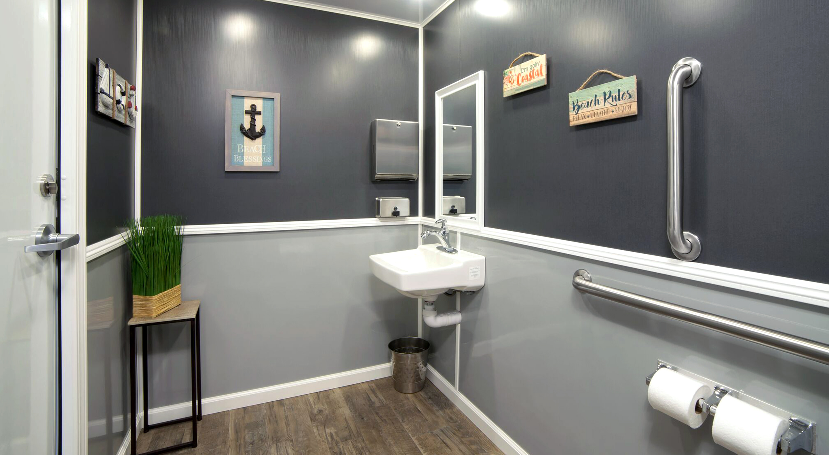Modern restroom featuring a sink, grab bar, decorative signs, and stylish gray walls.