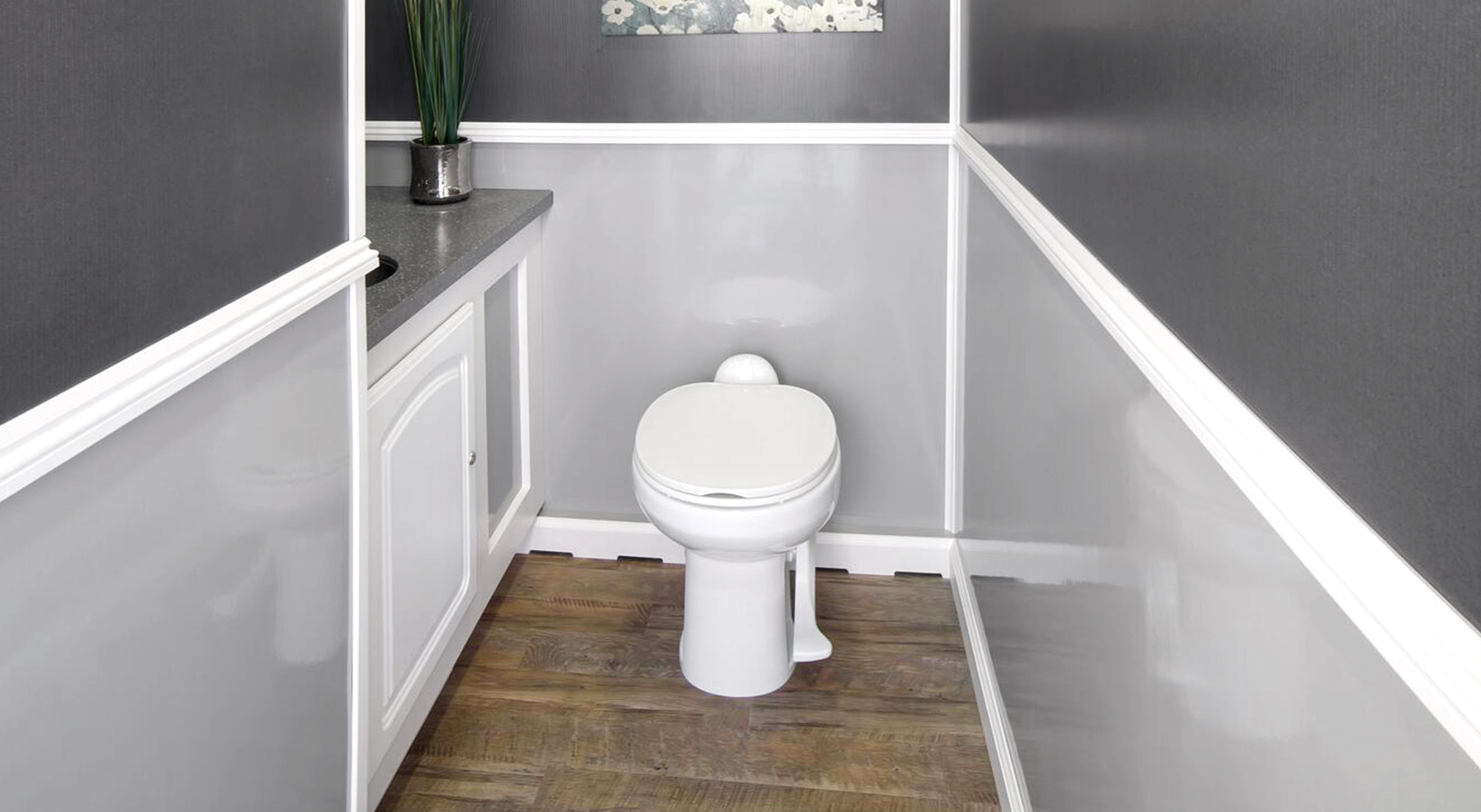 Small modern restroom with white toilet, wood floor, gray walls, and white cabinetry with plant.