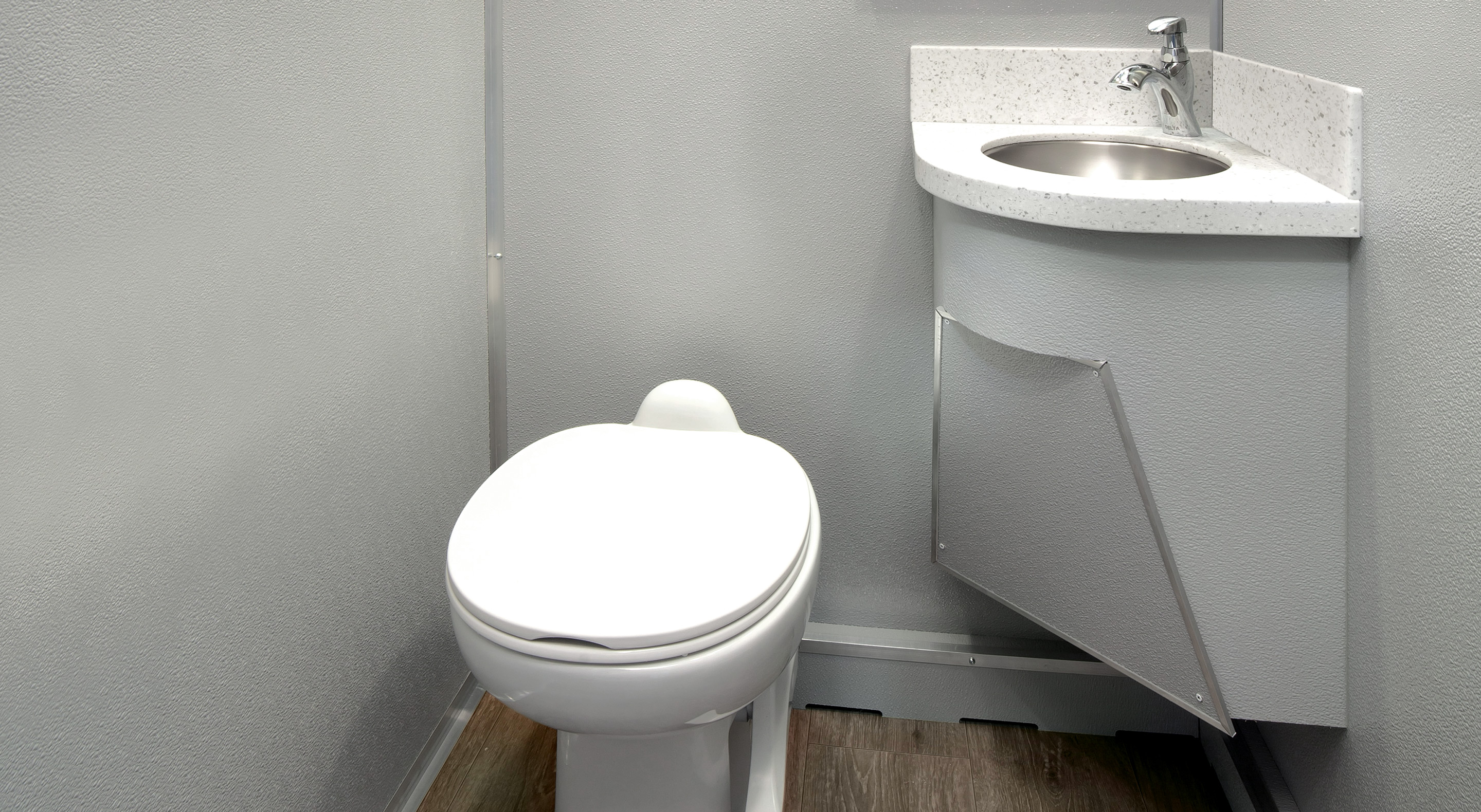Compact toilet with closed lid next to corner sink in a small gray textured bathroom.