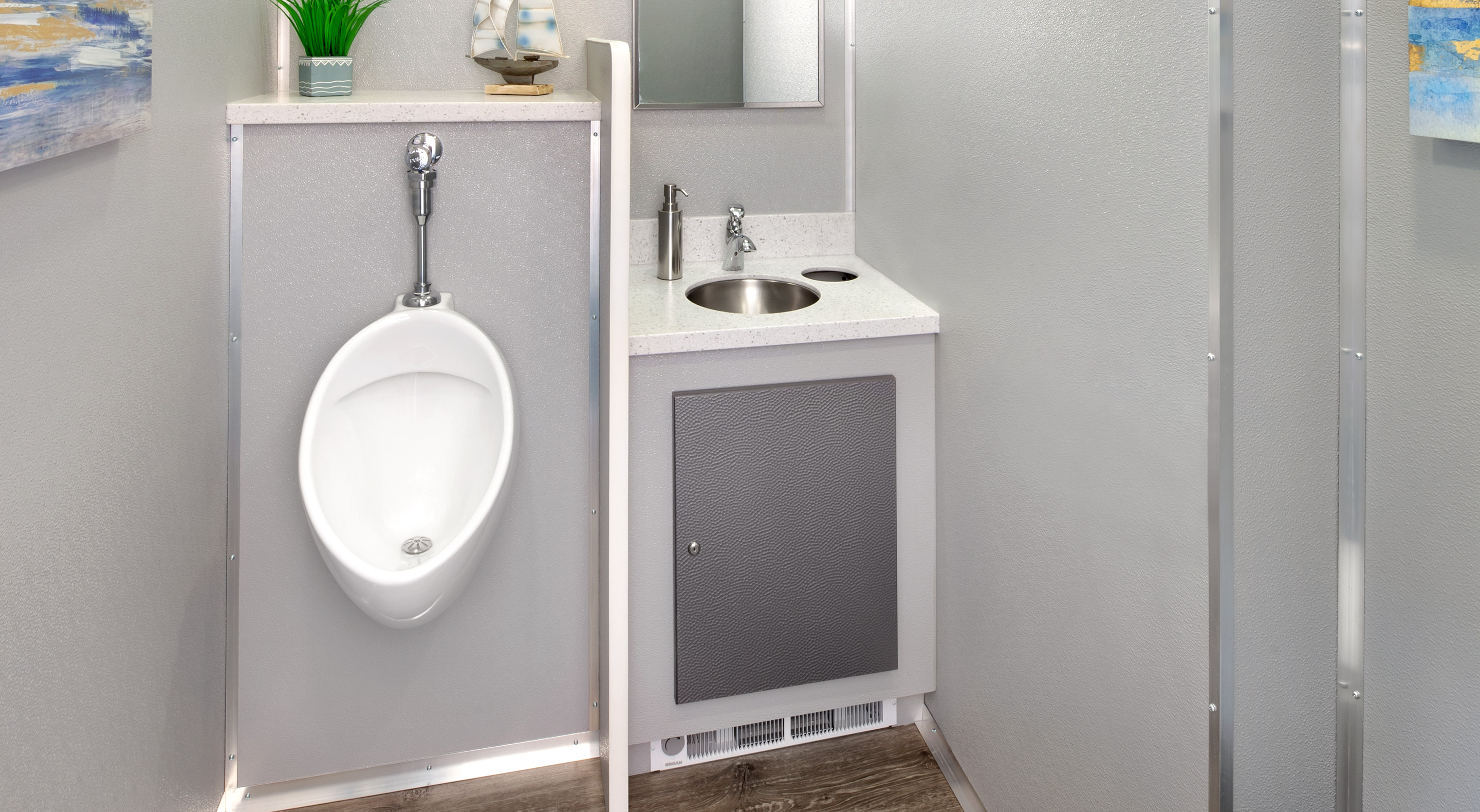 Men's restroom with a white urinal, sink, and mirror against a gray wall.